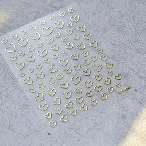 Detalle de pegatinas para uñas de corazón dorado con acabado metálico sobre base clara