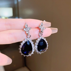 Detail view of silver drop earrings featuring a blue pear-cut stone with zircon halo