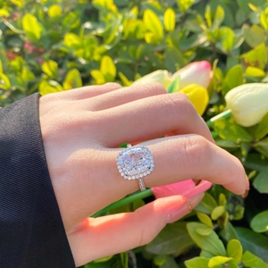 Close-up of cushion-cut halo ring with pavé diamonds on a hand with flowers