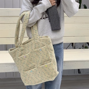 Detail of knit tote bag with four front pockets and colorful buttons on white bench