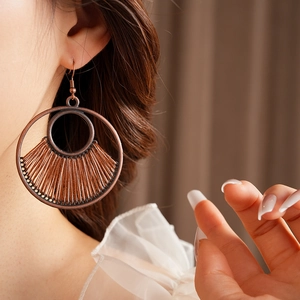 Detail of vintage round hollow earrings with bronze metal and brown woven thread on model