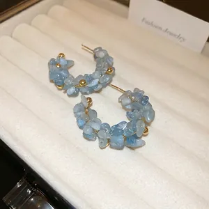 Handmade C-shaped hoop earrings with light blue beads and gold accents in a white box