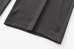 Détail du pantalon gris foncé montrant la texture en sergé et l'ourlet surpiqué