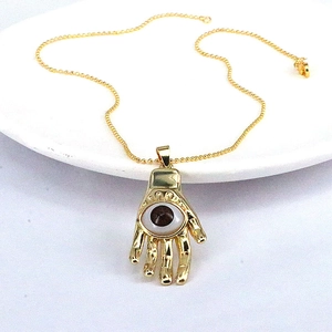 Detailed close-up of golden bead chain necklace with resin eye and Hamsa hand pendant