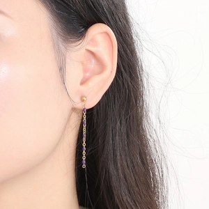 Macro view of long gold tassel earrings with small purple resin beads on a model