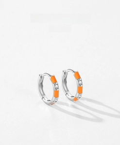 Macro shot of silver ear hoop featuring vibrant orange enamel and inlaid cubic zirconia