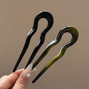 Close-up of glossy wave-shaped U-style resin hair pins in black and deep emerald green