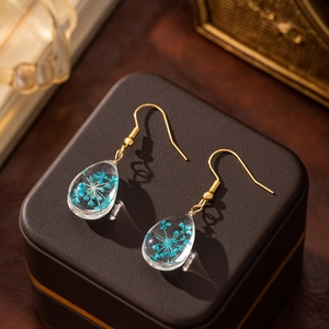 Macro detail of teardrop resin earring with blue dried flowers on a jewelry box