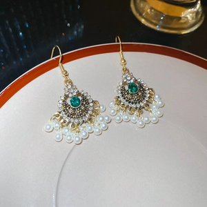 Dettaglio di orecchini vintage dorati con gemme verdi e perle bianche pendenti