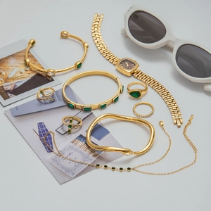 Gold-plated jewelry set with green stones and square watch on minimalist background