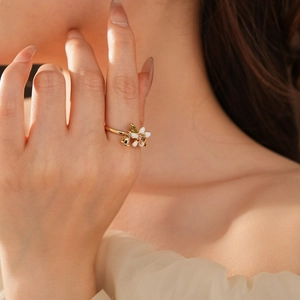 Dettaglio di un anello a fiore bianco placcato oro con foglia verde indossato da una modella