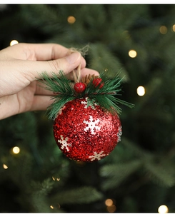 Detailed view of a red glitter Christmas ball with silver snowflakes, pine cones and berries