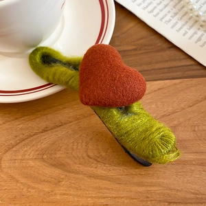 Detail of green knit hair clip with red felt heart decoration on a wooden background