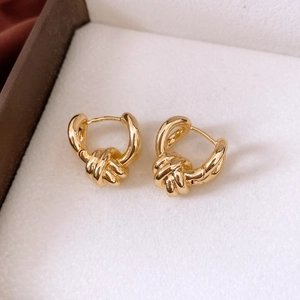 Detail view of gold twisted knot hoop earrings on a soft white velvet jewelry box surface