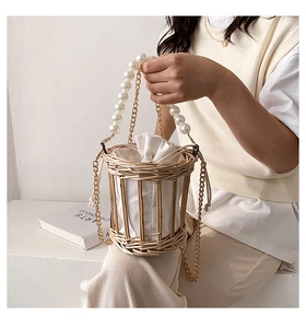 Detail of hand-woven straw bucket bag with pearl handle and golden chain strap
