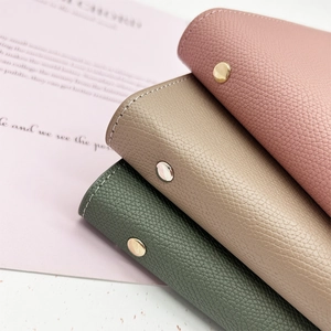 Close-up of lychee grain leather notebooks in pink, tan, and green with metal snaps