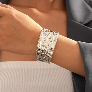 Dettaglio del bracciale rigido argento con trama lavica abbinato a un blazer grigio