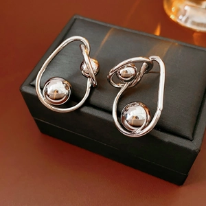 Macro shot of silver metallic twisted hoop earrings with spherical beads on black box