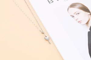 Macro shot of a polished silver heart-shaped key pendant on a delicate link chain necklace