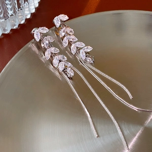 Macro shot of silver leaf earrings with rhinestone tassels on a metal tray