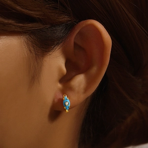 Detail of gold turquoise huggie earring with blue enamel and zircon on the earlobe