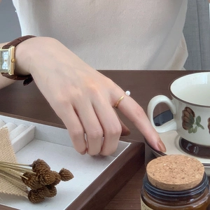 Detailed view of an elegant gold pearl open ring paired with a vintage square watch