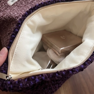 Close-up of woven tweed makeup bag in soft purple with beige lining and metal zipper