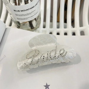 Elegante pinza per capelli in acrilico bianco con scritta 'Bride' in cristallo su libro