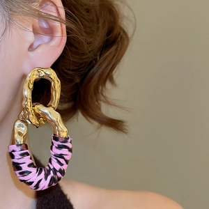 Detail of geometric gold metal ring interlocking with a pink and black leopard print leather drop
