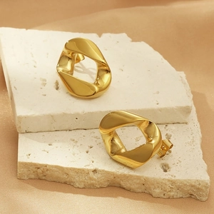 Dettaglio di orecchini geometrici intrecciati in oro su pietra bianca con texture