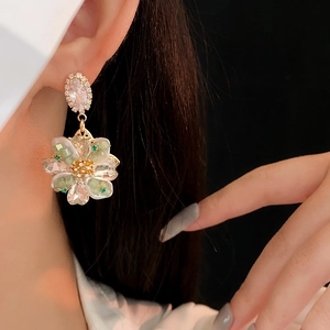 Détail de boucles d'oreilles fleurs en or avec cristaux verts portées par un mannequin