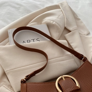 Close-up of caramel brown pebble leather underarm bag with gold metal buckle detail