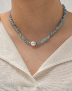 Close-up of model wearing a necklace with light blue stones and a white pearl accent