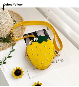 Detail of yellow strawberry shaped crossbody bag with green leaf decor on a summer table