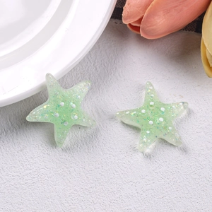 Macro detail of light green resin starfish earrings with glitter and cute white dot patterns