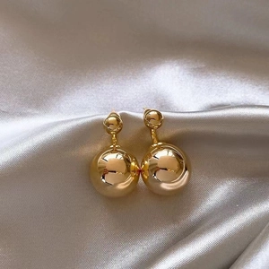 Polished gold sphere dangle earrings displayed on elegant beige silk fabric background