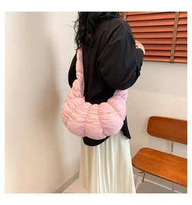 Pink pleated cloud bag shown on model's shoulder in a warm lifestyle setting