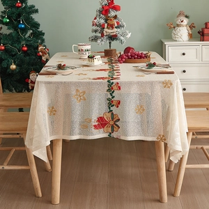 Detail of beige lace Christmas tablecloth featuring red bell and snowflake knit patterns
