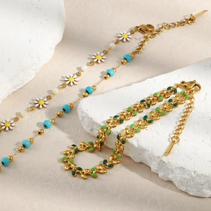 Detailed shot of 18K gold plated daisy beads and green enamel leaf bracelet on white stone