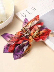 Detail of paisley print bow hair claw clip with vibrant purple and orange gradient fabric