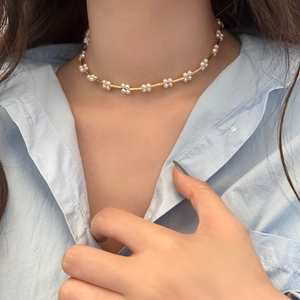 Detail of a gold braided necklace featuring delicate pearl flower charms on a model