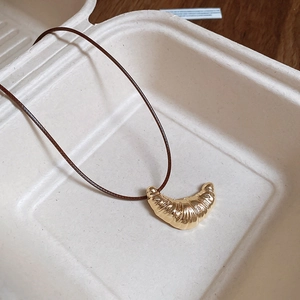 Macro detail of golden croissant pendant with brown cord inside eco-friendly packaging