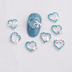 Light blue heart nail art charms with rhinestones and silver bow on blue nail model