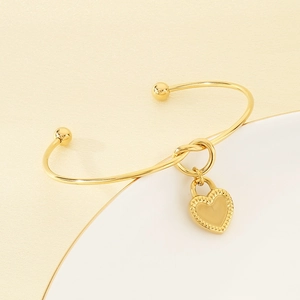 Detail of gold knot cuff bracelet with textured heart charm on minimalist background