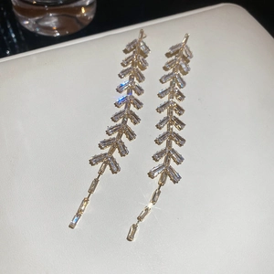 Vue macro de boucles d'oreilles feuilles en zircon doré sur surface en cuir texturé
