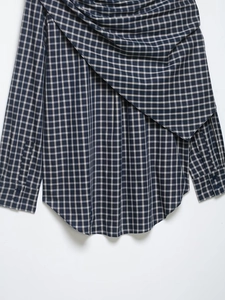 Detail of plaid long sleeve shirt featuring asymmetric draped front folds and woven texture