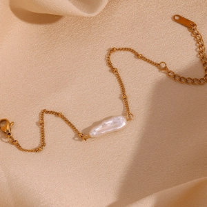 Detail of 18K gold plated chain bracelet with a white baroque pearl on beige fabric
