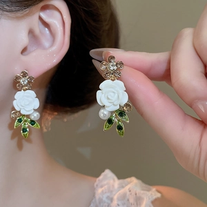 Close-up of floral earring with white rose, green leaf accents and a hanging pearl