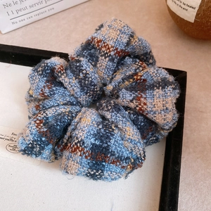 Vue détaillée d'un chouchou en tweed à carreaux bleu et marron sur un plateau élégant