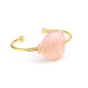 Detail eines handgefertigten Armreifens mit herzförmigem rosa Kristall und Lebensbaum